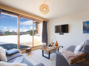 Una sala de estar moderna con un amplio ventanal corredera que da a un área exterior nevada, un televisor de pantalla plana montado en la pared y un sofá acogedor con una manta mullida.