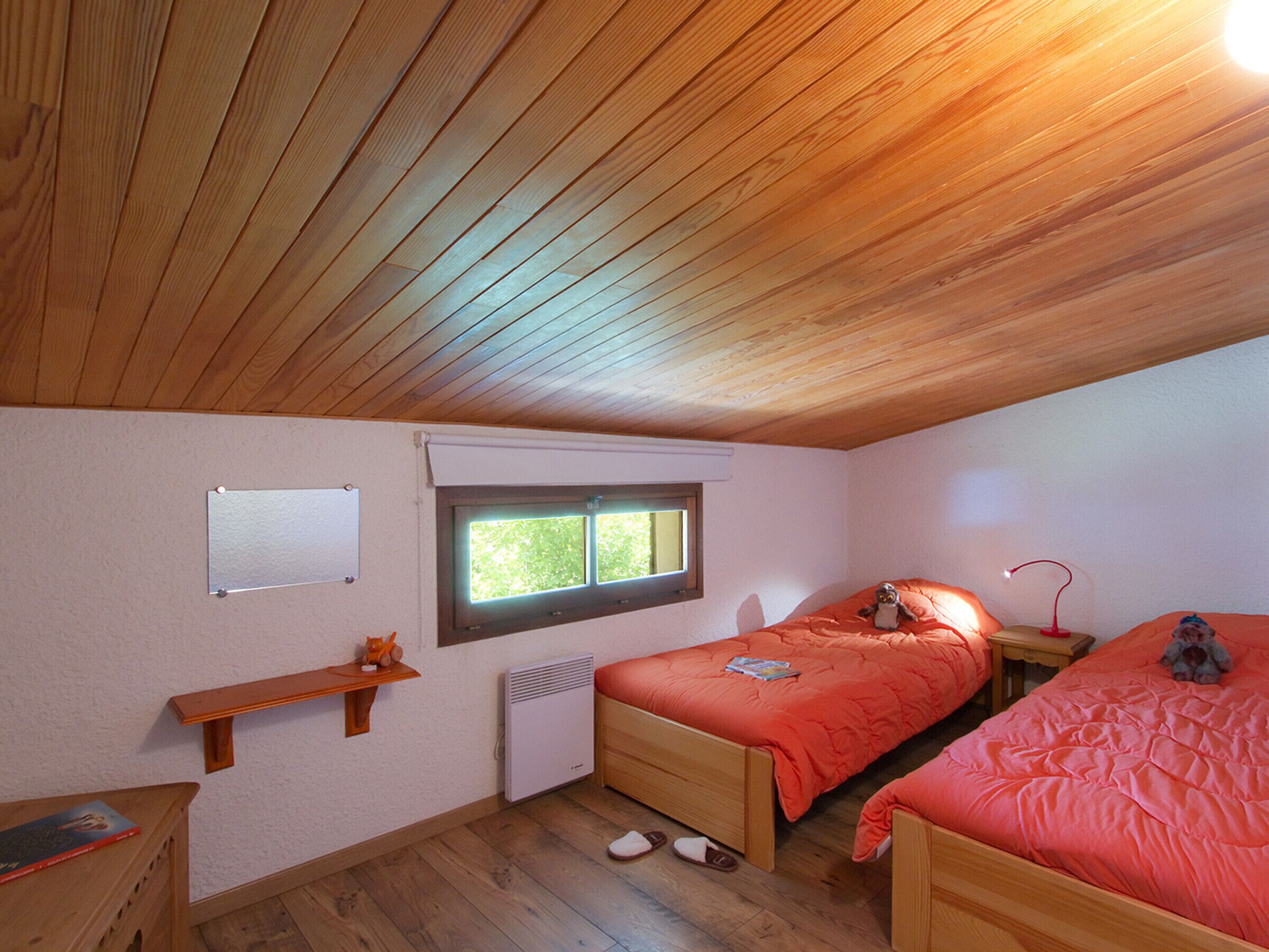 Un dormitorio con dos camas, una ventana, un calentador, un estante con un juguete y un escritorio con un libro.