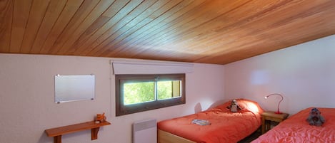 Un dormitorio con dos camas, una ventana, un calentador, un estante con un juguete y un escritorio con un libro.