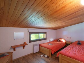 A bedroom with two beds, a window, a heater, a shelf with a toy, and a desk with a book. - Spacious apartment, ski-in ski-out access (Les Deux Alpes)