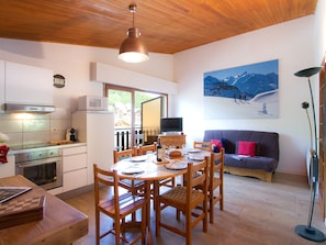 A dining area with a wooden table and chairs, a kitchen with a microwave and oven, a television, and a painting of a mountain landscape. - Spacious apartment, ski-in ski-out access (Les Deux Alpes)