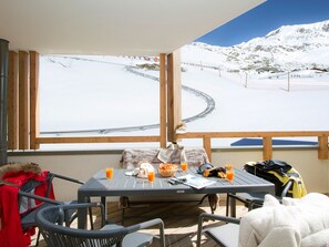 A table with chairs, a view of a snowy mountain, and a ski lift in the background. - Modern apartment at the foot of the slopes (Huez)