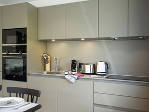 A modern kitchen with built-in appliances, a sink, and a dining area with a chair and table. - Modern apartment at the foot of the slopes (Huez)