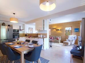 A modern kitchen with stainless steel appliances, a dining area with a wooden table and chairs, and a living space with a sofa and armchairs. - Spacious apartment, terrace, serene - 6 guests (Les Deux Alpes)