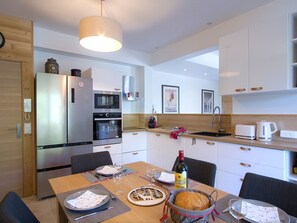A modern kitchen with stainless steel appliances, a dining table set for two, and a wine bottle on the table. - Spacious apartment, terrace, serene - 6 guests (Les Deux Alpes)