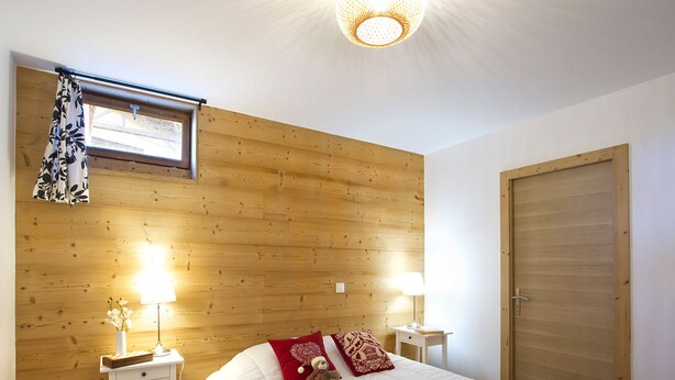Ein Schlafzimmer mit hölzernem Kopfteil, einem Bett mit weißer Bettwäsche, zwei Nachttischen mit Lampen, einem Fenster mit Vorhängen und einer Tür.