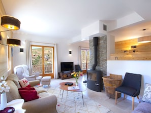 A spacious living room with a fireplace, comfortable seating, a television, and a view through large windows. - Spacious apartment, terrace, serene - 6 guests (Les Deux Alpes)