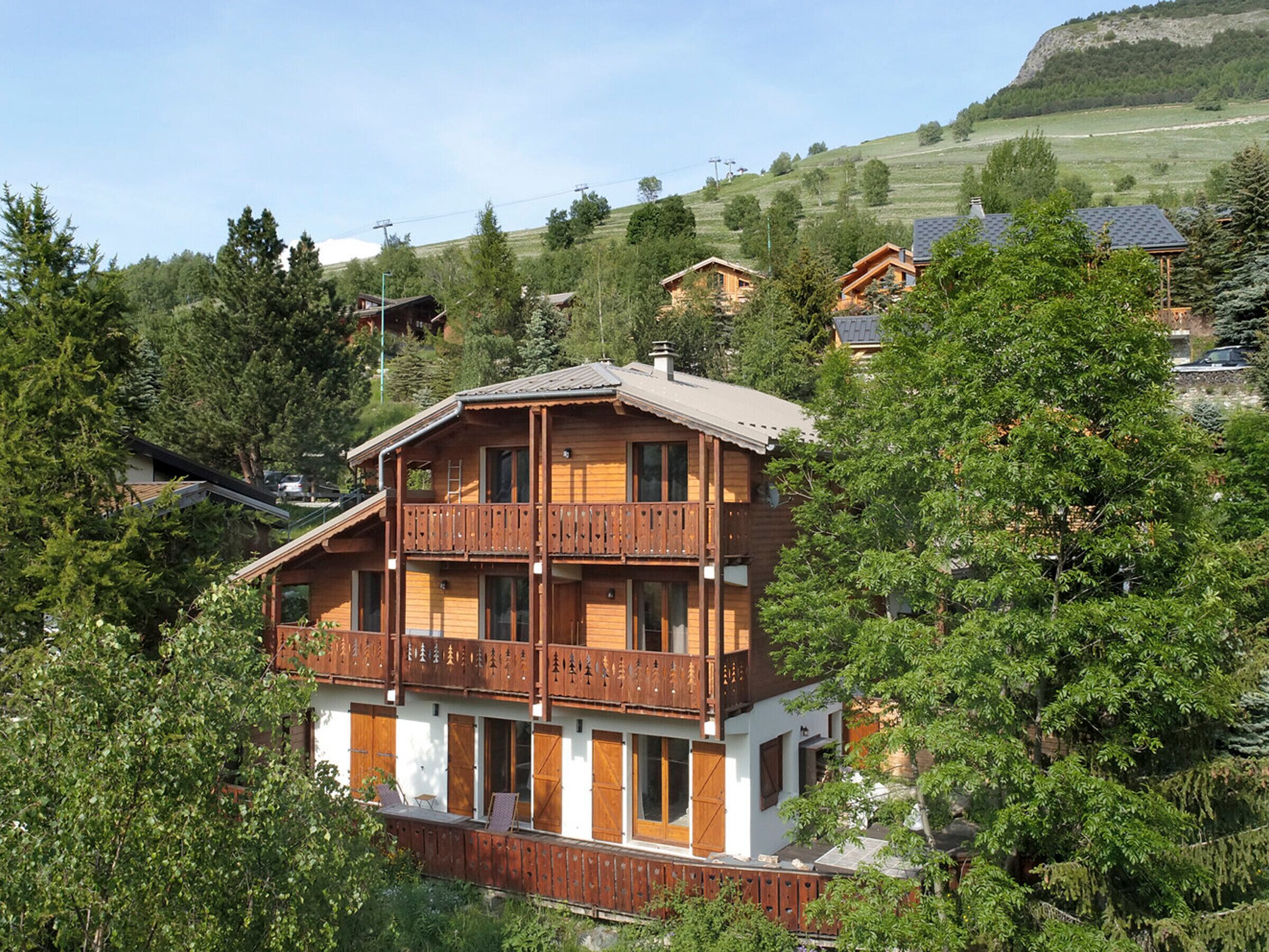 A multi-story wooden building with balconies, surrounded by trees and set in a hilly area.