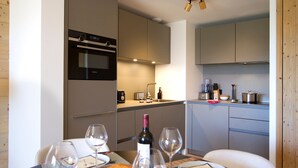 A compact kitchen with modern appliances, a dining table set with wine glasses and a loaf of bread. - Spacious apartment with garden - 5 guests (Huez)