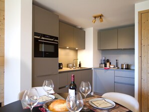 A compact kitchen with modern appliances, a dining table set with wine glasses and a loaf of bread. - Spacious apartment with garden - 5 guests (Huez)