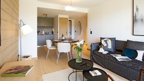 A modern living room with a grey sofa, a coffee table, and a dining area with chairs and a table. - Spacious apartment with garden - 5 guests (Huez)