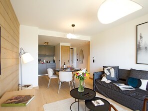 A modern living room with a grey sofa, a coffee table, and a dining area with chairs and a table. - Spacious apartment with garden - 5 guests (Huez)