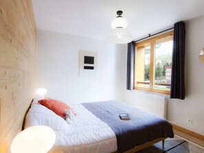 A bedroom with a bed, a window, a radiator, and a wall-mounted light fixture. - Spacious apartment near slopes - pers. (Les Deux Alpes)