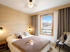 A bedroom with a bed, a window with a view of a snowy landscape, a chair, and a lamp. - Spacious apartment mountain view - 4 guests (Huez)