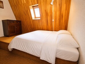 A bedroom with a wooden sloped ceiling, a single bed with white bedding, a nightstand, and a small window. - Duplex with parking - 4 guests, stunning view (Les Deux Alpes)