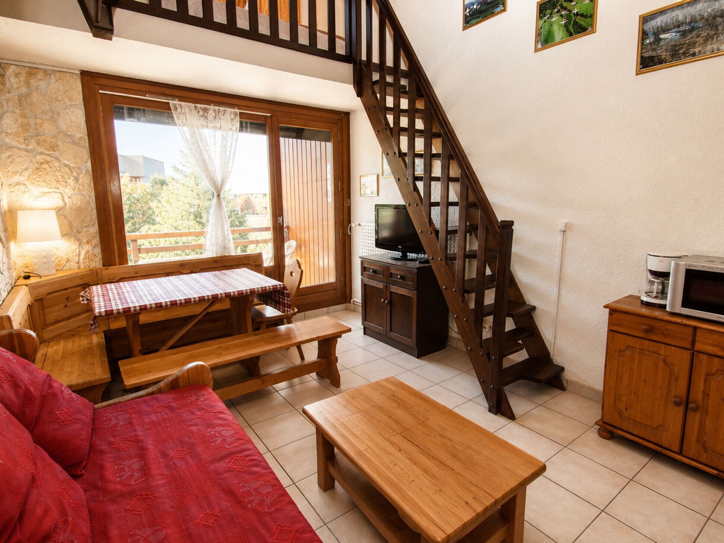 A cozy living room with a wooden staircase, a television, and a dining area with a table and benches.