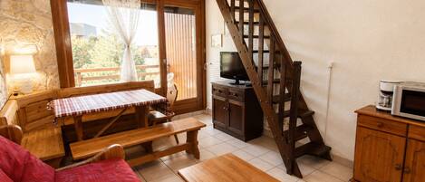 Una sala acogedora con una escalera de madera, un televisor y una zona de comedor con una mesa y bancos.