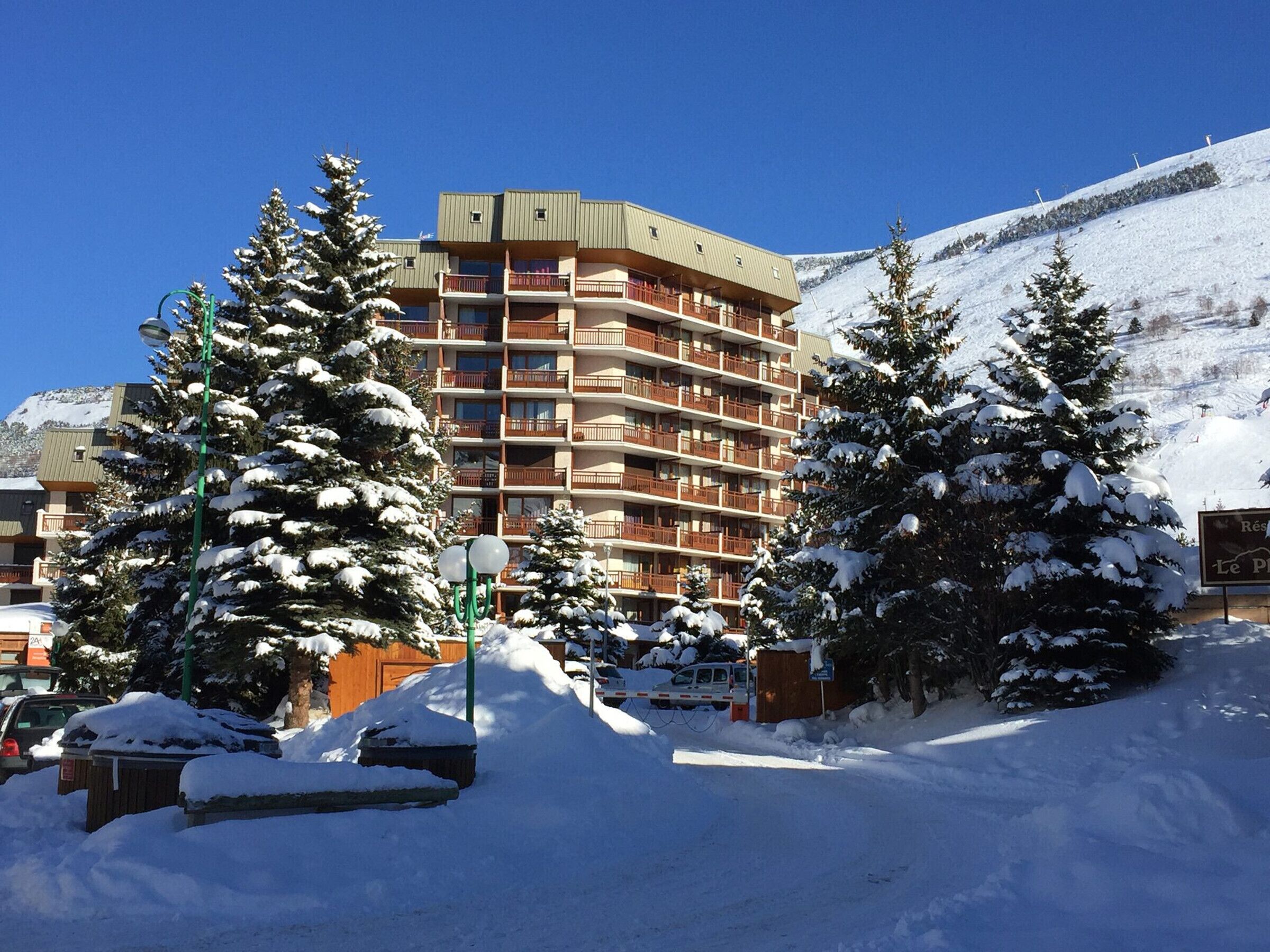 A multi-story hotel with balconies, surrounded by snow-covered trees and a mountain in the background.