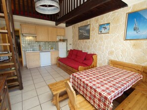 A compact kitchen with wooden cabinets, a white refrigerator, and a stone wall with framed pictures. - Duplex with parking - 4 guests, stunning view (Les Deux Alpes)