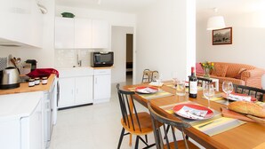 Una cocina moderna con armarios blancos, un microondas y un comedor con una mesa de madera dispuesta para dos.