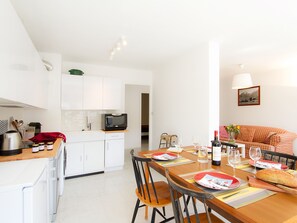 Eine moderne Küche mit weißen Schränken, einer Mikrowelle und einem Essbereich mit einem Holztisch, gedeckt für zwei Personen.