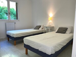 A bedroom with two single beds, a bedside table with a lamp, and a window with a view of greenery. - Bright apartment, mountain view - 4 guests (Les Deux Alpes)