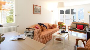Una sala de estar con sofá, una mesa y vistas a montañas a través de las ventanas.