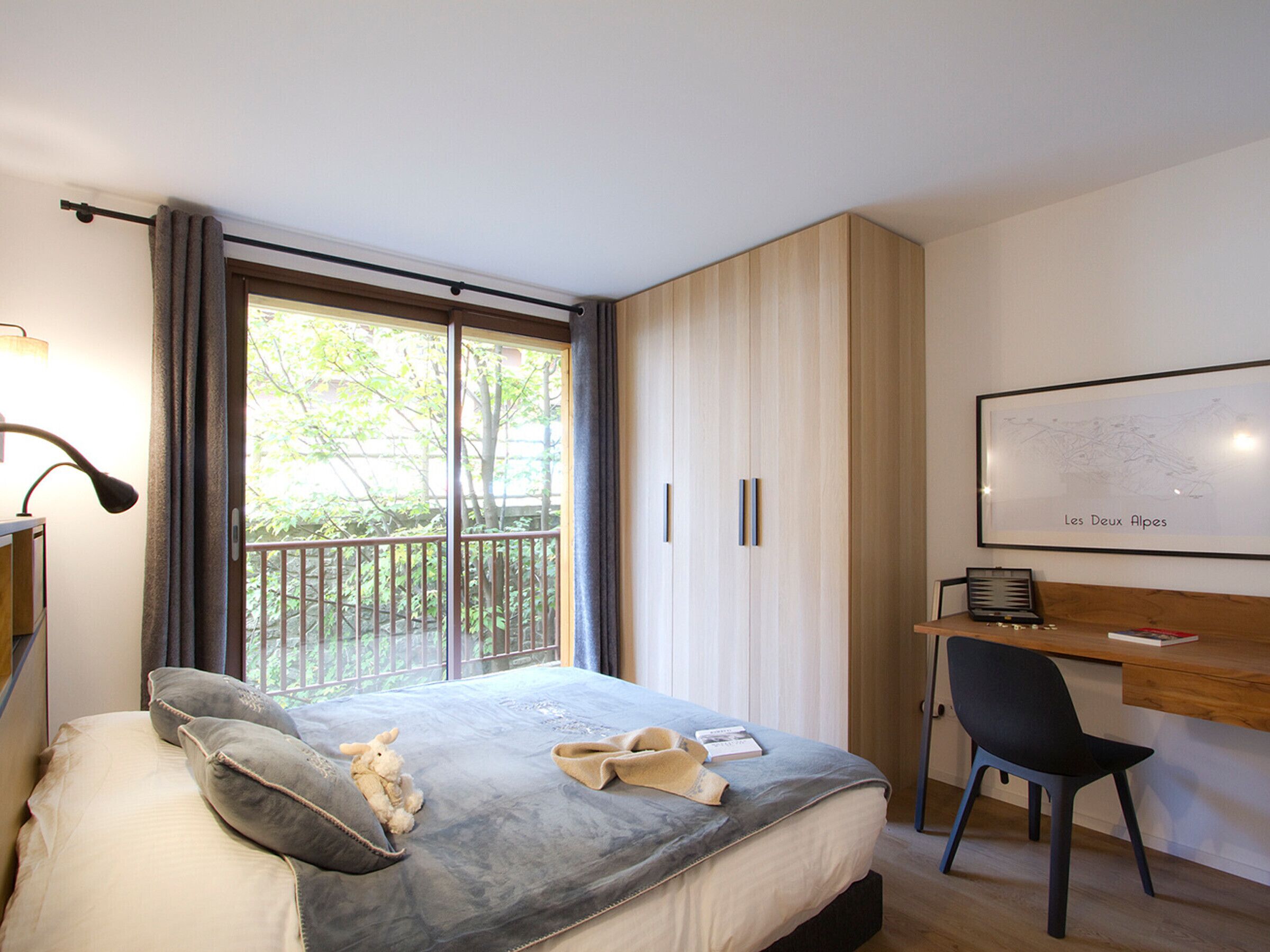 Un dormitorio con cama, escritorio, silla, ventana con cortinas y un mapa enmarcado en la pared.