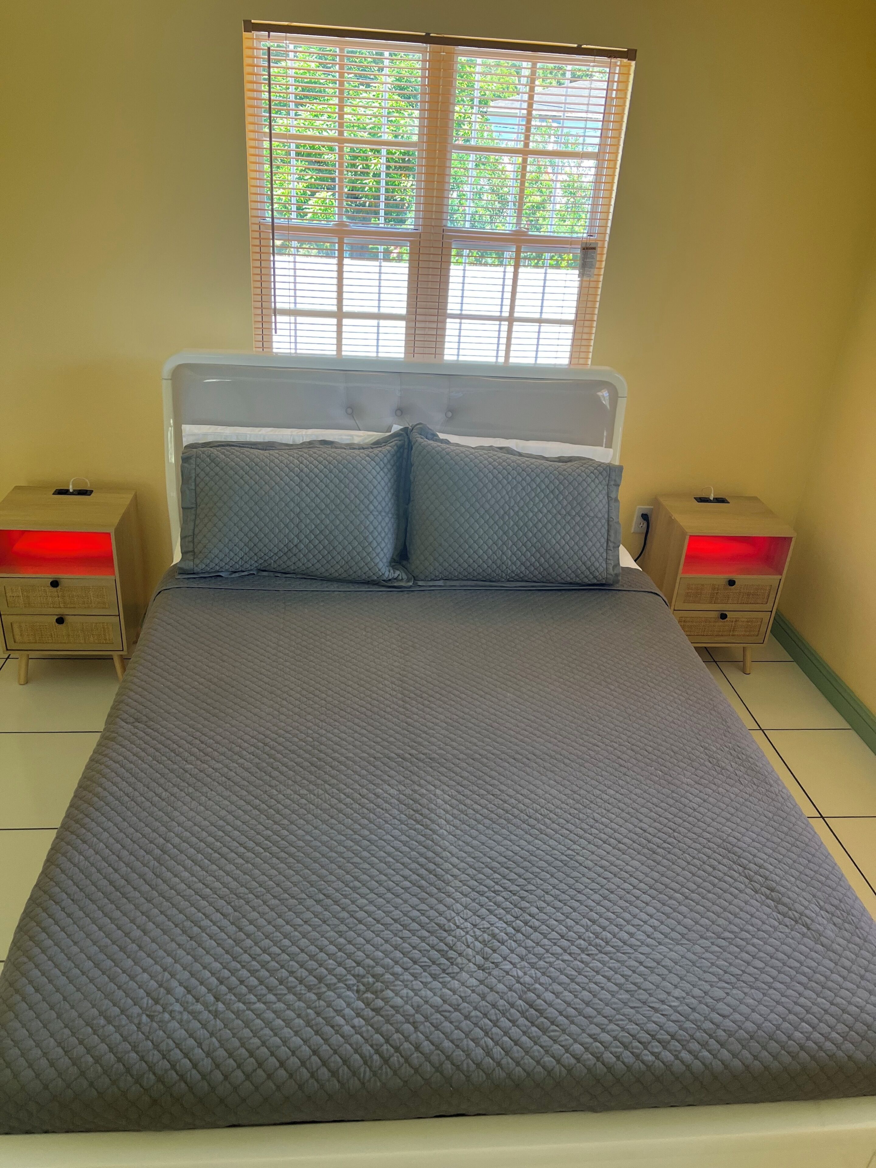 Uma cama com cobertura acolchoada, duas almofadas, uma cabeceira e duas mesas de cabeceira com abajures.