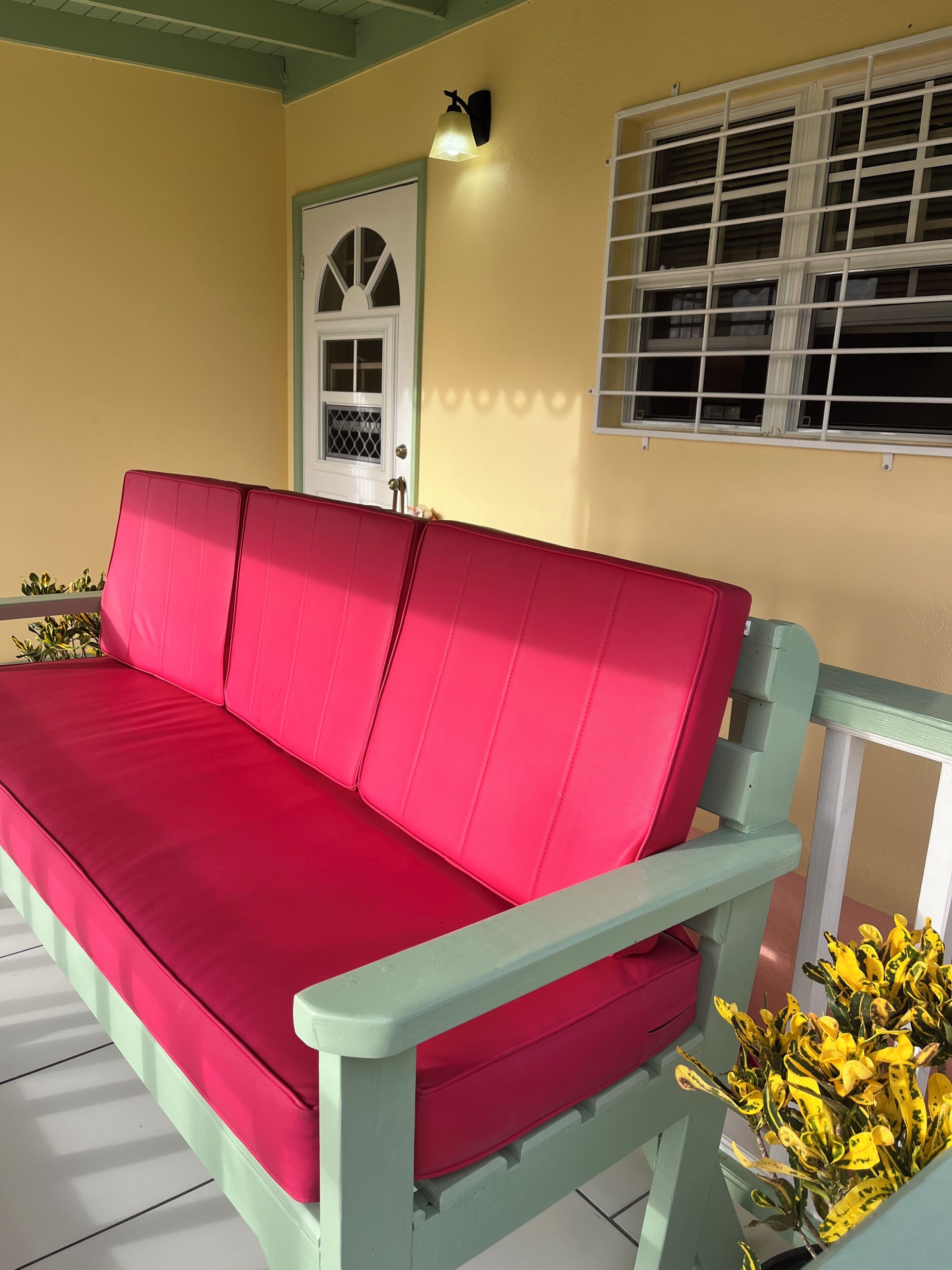 A red sofa with a light green frame, a white door with a window, and a window with horizontal bars.