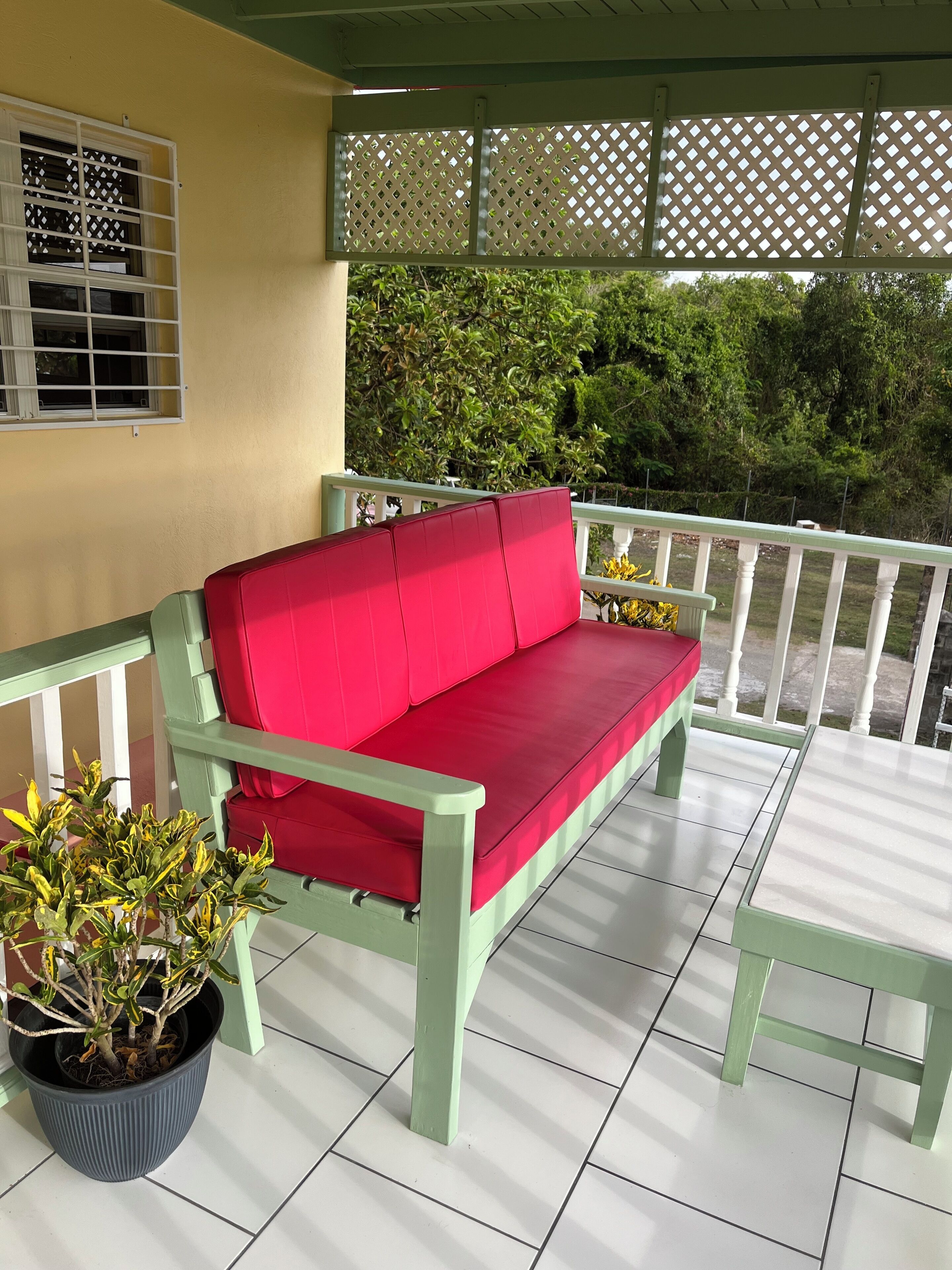 Un espacio de estar techado al aire libre con un sofá rojo, una silla verde y una planta en maceta.