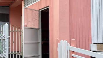 Un bâtiment à la façade rose, avec une clôture blanche et une porte entrouverte donnant sur un espace intérieur.