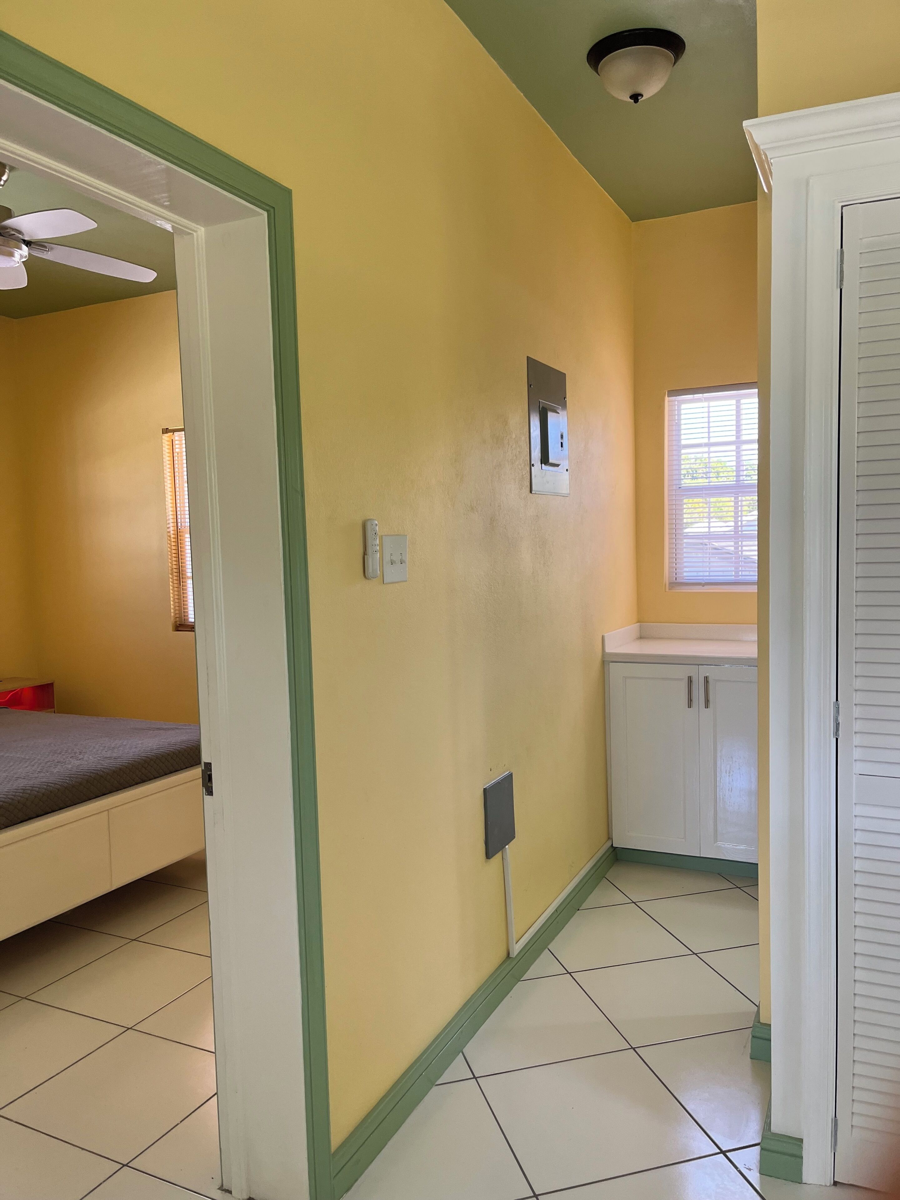 Una habitación con cama, ventana, puerta y una lámpara fijada a la pared.