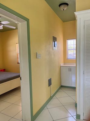 Una habitación con cama, ventana, puerta y una lámpara fijada a la pared.