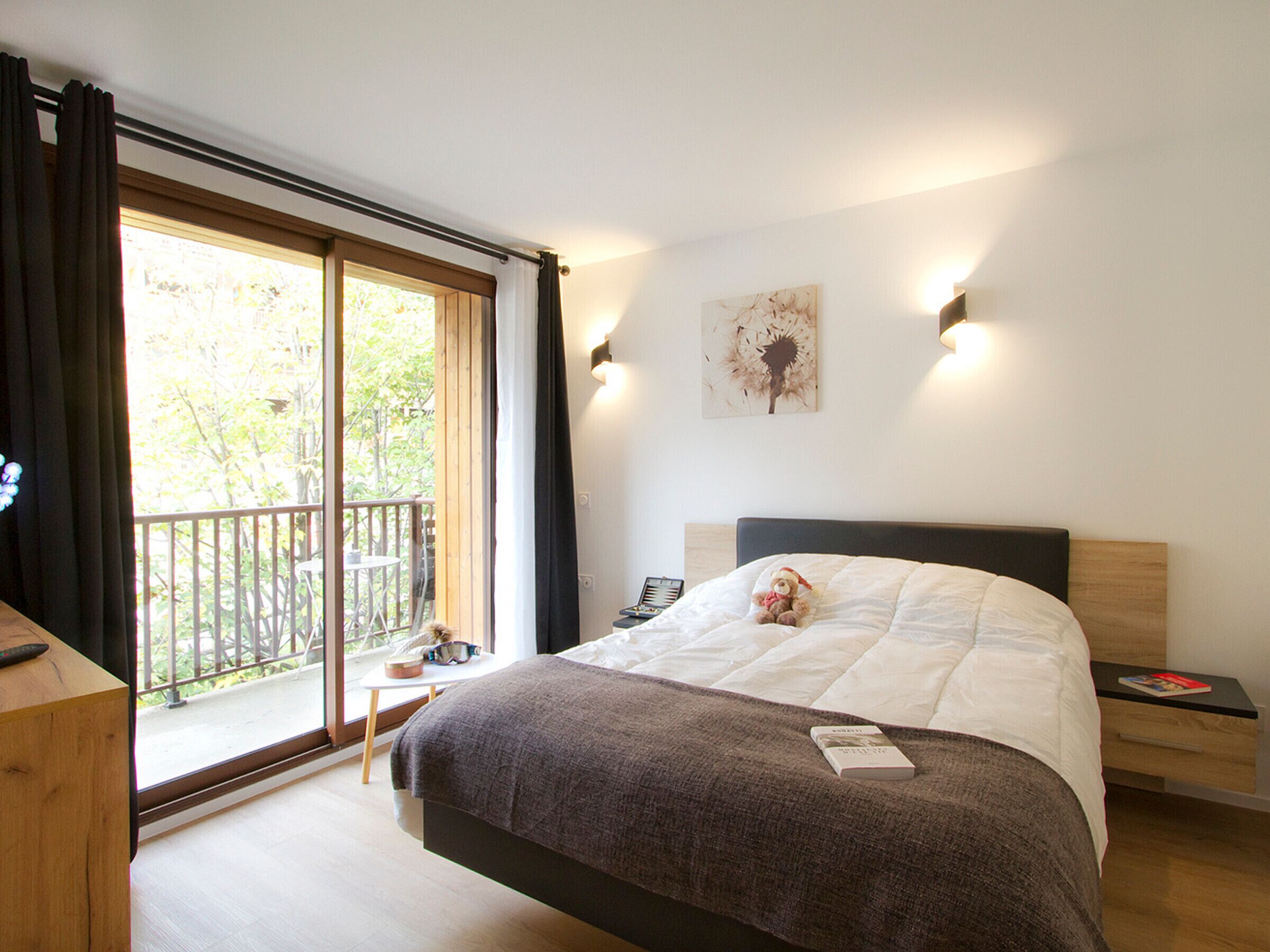Un dormitorio con cama, mesita de noche, cortinas y vistas al exterior.