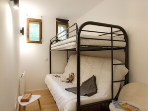 Ein Stockbett mit einem Fenster, ein kleiner Tisch mit Schachbrett und eine Zeitschrift auf dem Bett.