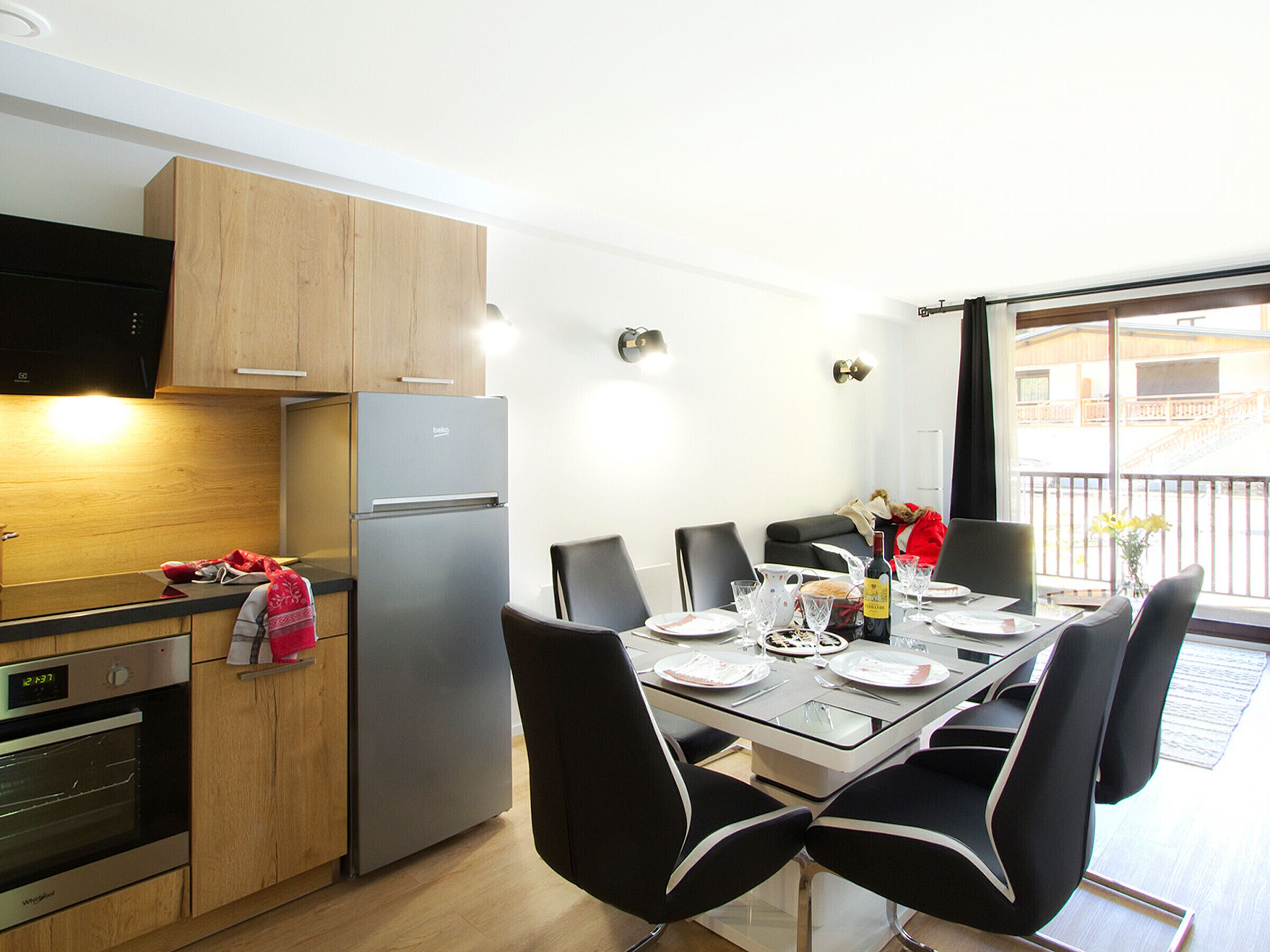 Eine moderne Küche mit Holzschränken, einem Edelstahlkühlschrank und einem Essbereich mit Glastisch und schwarzen Stühlen.