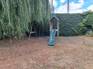 A playground with a slide and swings, surrounded by a hedge and a tree. - Charming house with a garden, ideal for families, close to shops and lakes (Brienne-le-Château)