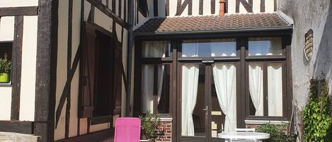 A traditional half-timbered building with a gravel courtyard, a pink chair, and a table.