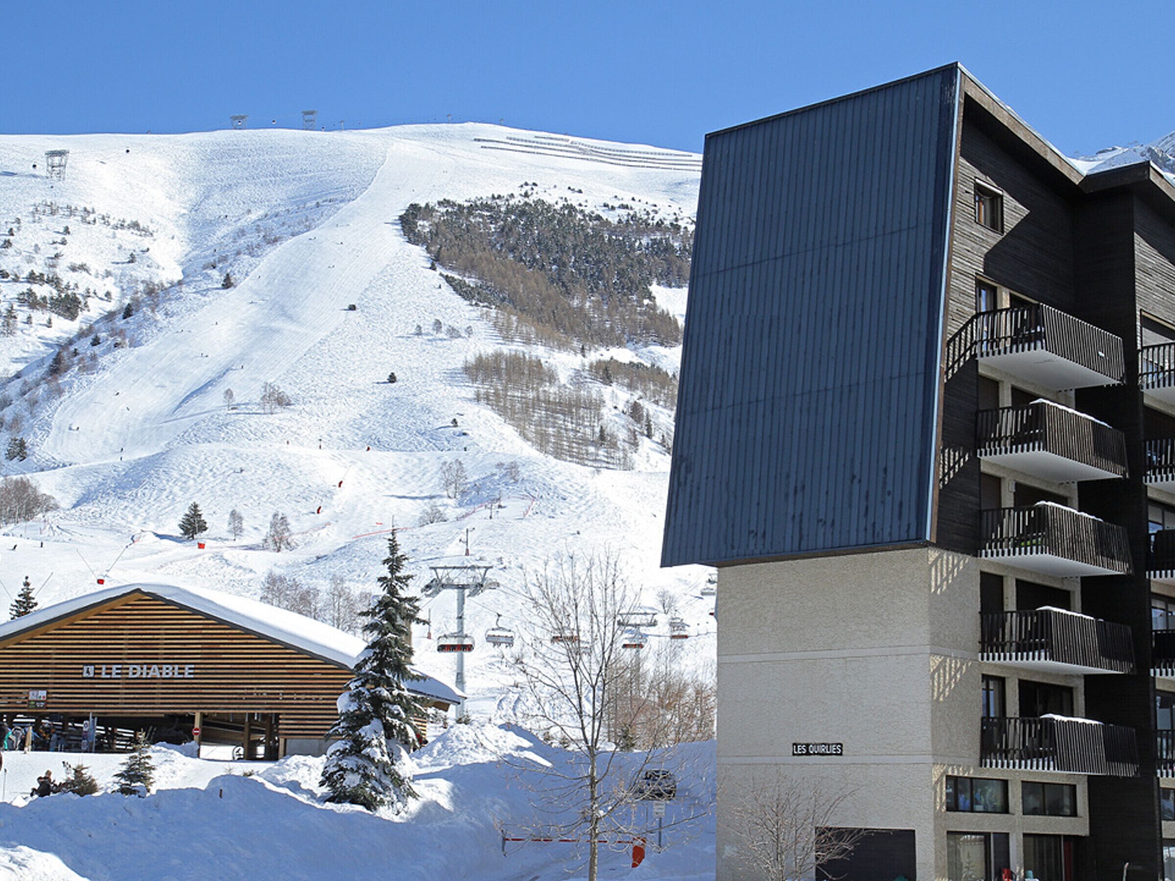 Une station de ski avec un bâtiment en bois portant l’inscription « LE DIABLE » et un immeuble d’appartements moderne doté de balcons.