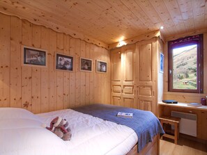 A wooden-paneled room with a bed, a desk, and a window with a view of a mountainous landscape. - Bright apartment at the foot of the slopes (Les Deux Alpes)