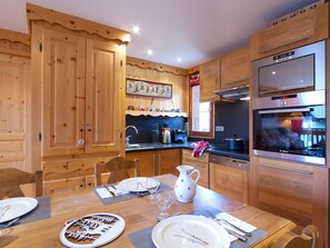 A wooden kitchen with a Bosch oven, wooden cabinets, and a dining table set for two. - Bright apartment at the foot of the slopes (Les Deux Alpes)