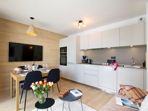 A modern kitchen with white cabinets, a dining area with a table and chairs, and a flat-screen TV mounted on the wall. - Apartment, ski-in/ski-out, piste view (Huez)