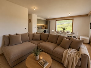 A modern living room with a large sectional sofa, a coffee table with a book and a plant, and a dining area with a view of the outdoors. - Spacious, comfortable apartment - 6 guests (Huez)
