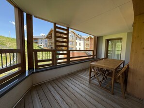 A balcony with a wooden table and chairs, a view of buildings, and a clear sky. - Spacious, comfortable apartment - 6 guests (Huez)