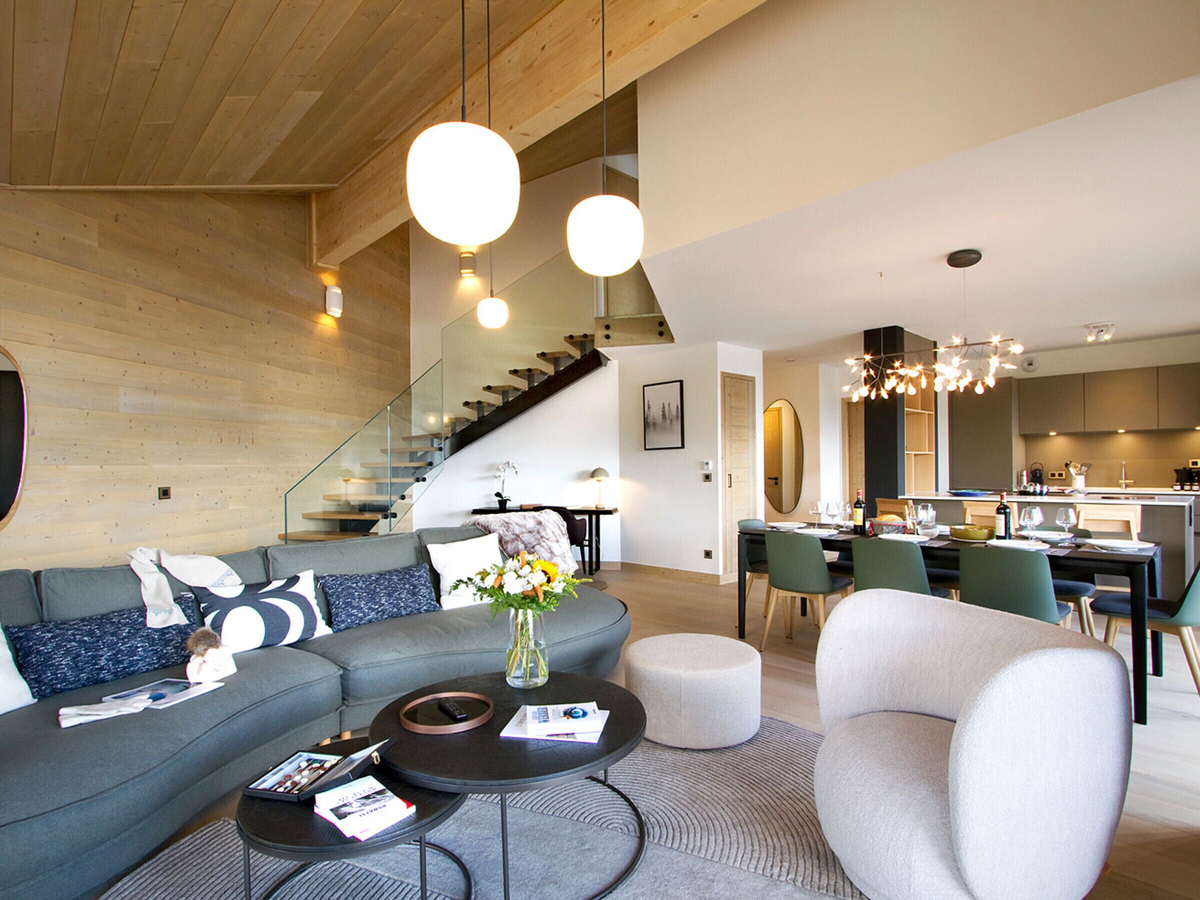 A modern living room with a sectional sofa, a round coffee table, and a dining area with a kitchen in the background.