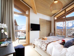 Ein Schlafzimmer mit Bett, Schreibtisch, Stuhl, Fernseher und Blick auf Berge durch große Fenster.