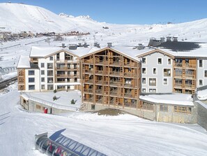 Ein mehrstöckiges Hotel mit Holzfassade, gelegen in einer verschneiten Berglandschaft mit Skipisten im Hintergrund.