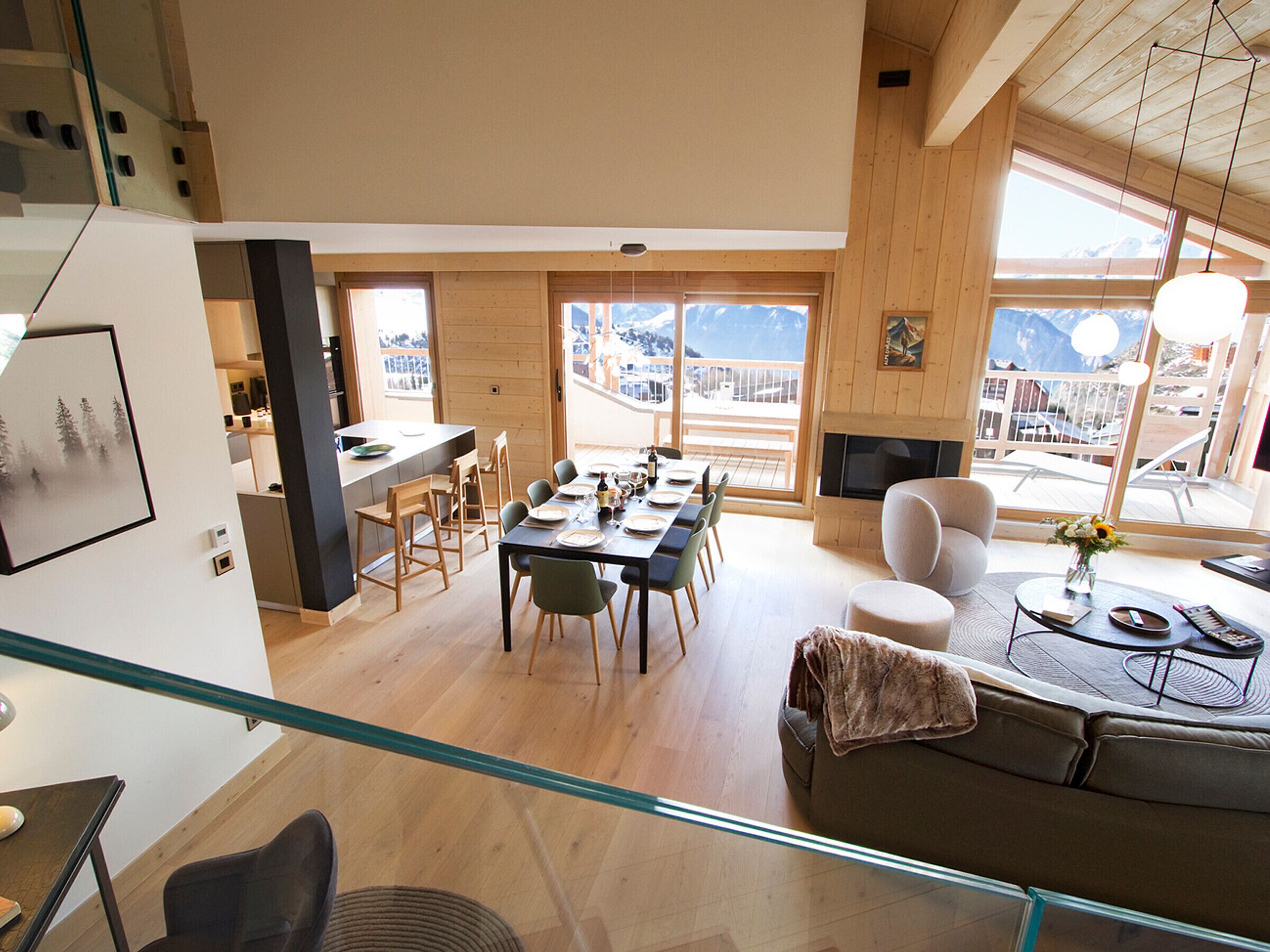 Amplia sala de estar con mesa de comedor, sillas y sofá. Hay una chimenea y ventanas grandes que ofrecen vistas a las montañas.