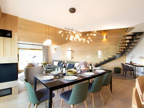 Ein moderner Essbereich mit einem langen Tisch, der für eine Mahlzeit gedeckt ist, umgeben von Stühlen. Im Hintergrund ist eine Treppe zu sehen.